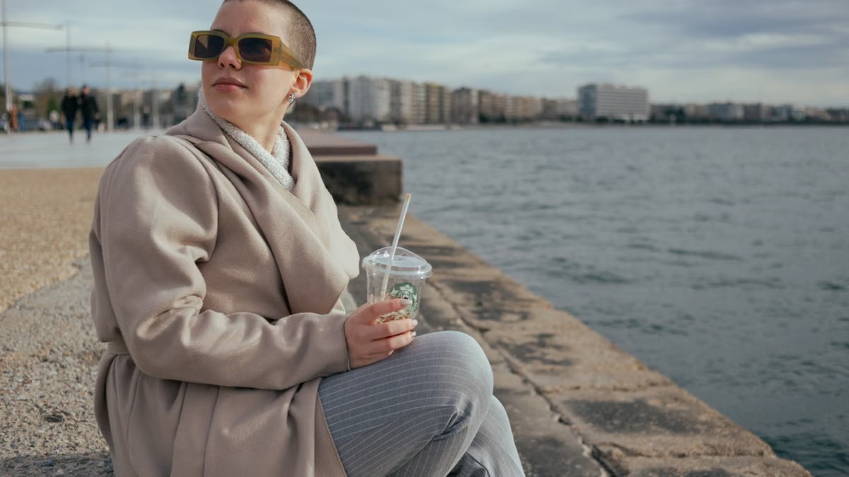 Woman in fashion coat by the seaside, enjoying leisure with a drink.